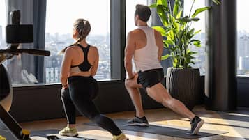 Et fitnesscenter med store vinduer, træningsudstyr og en potteplante.