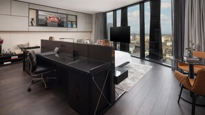 A modern hotel room with a large desk, a comfortable chair, a bed, and a large window offering a city view. - art'otel London Hoxton (London)