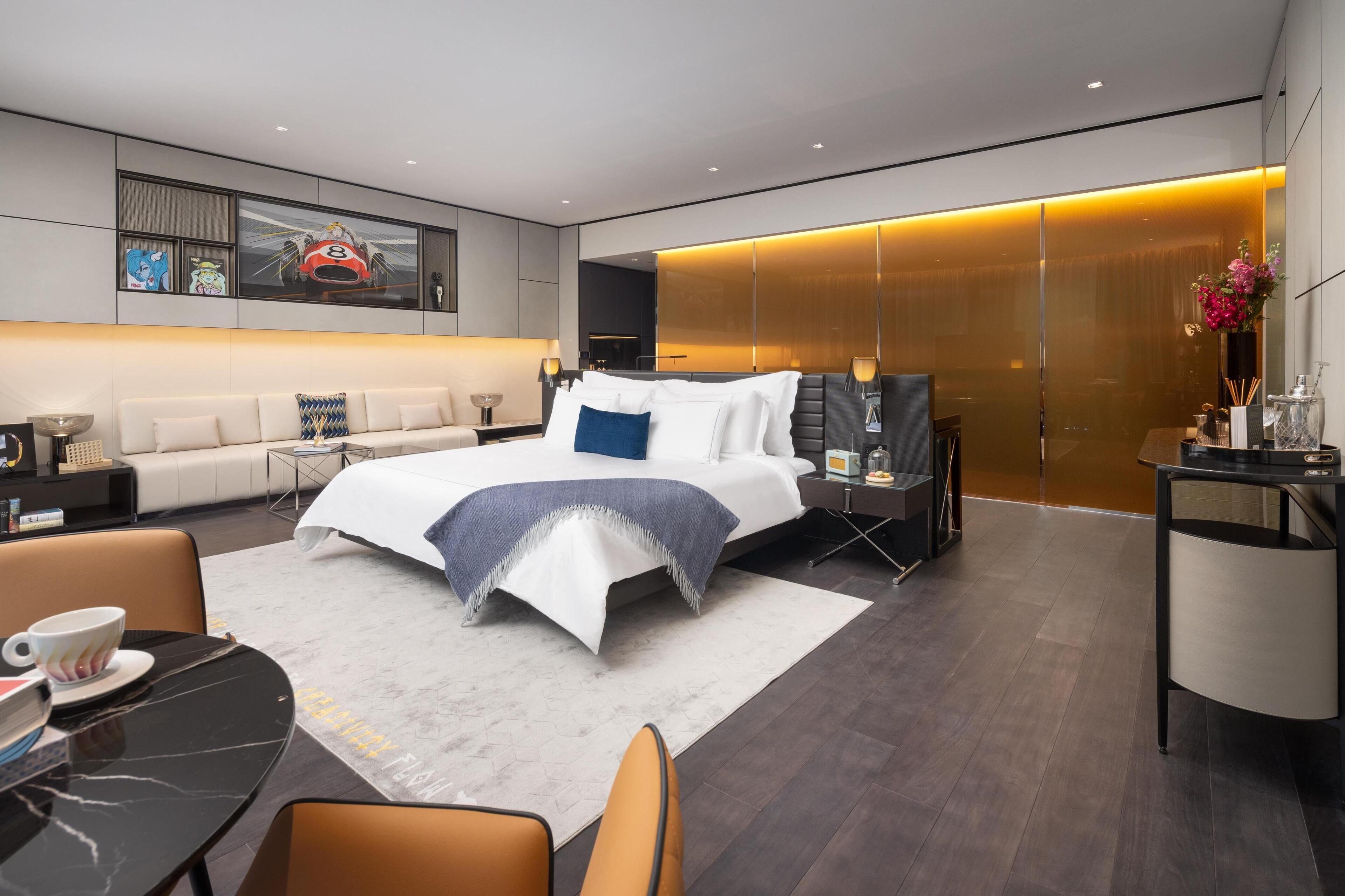 Una habitación de hotel moderna con una cama grande, una zona de estar, un escritorio y un ventanal amplio.