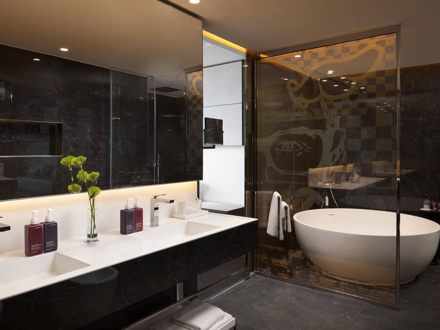 Une salle de bain moderne avec un grand miroir, un lavabo blanc et une baignoire sur pieds.