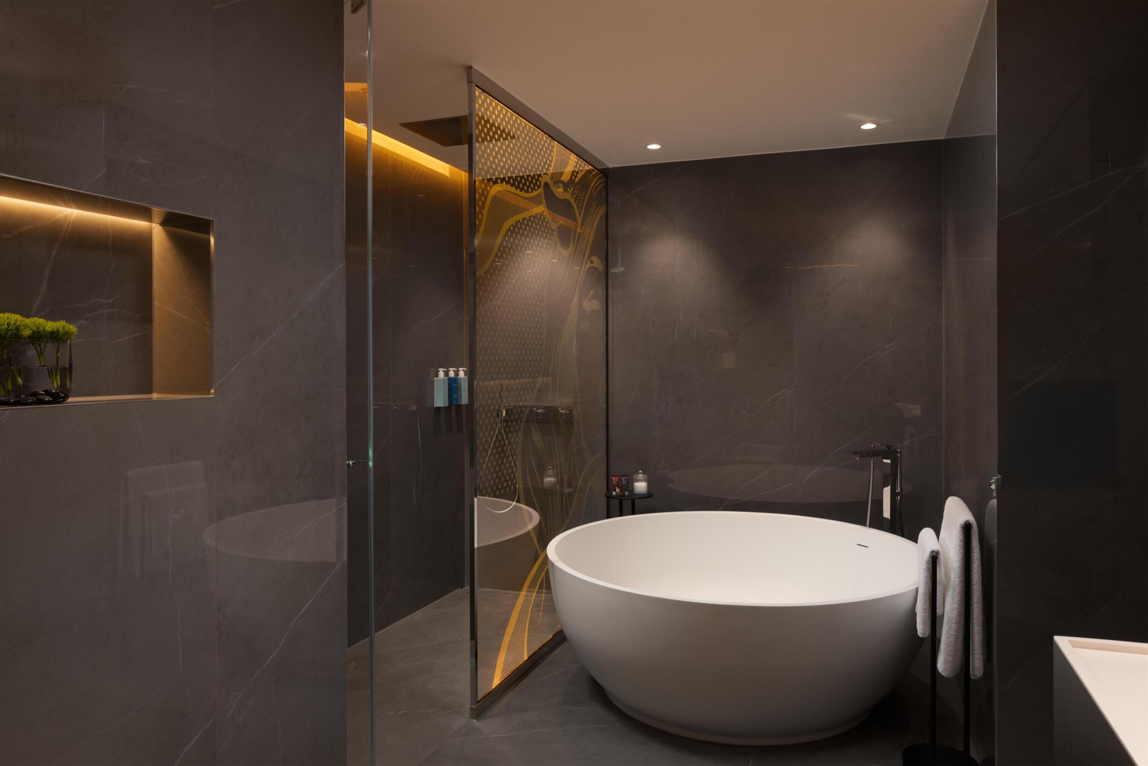 Un baño moderno con una bañera independiente, ducha con mampara de vidrio y una zona pequeña para el lavamanos.