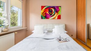 Un dormitorio con una cama grande, un cuadro abstracto y colorido en la pared, y una ventana con cortinas blancas.