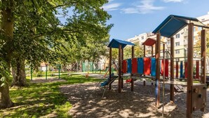 Un parque infantil con estructuras para escalar y un tobogán, rodeado de árboles y edificios.