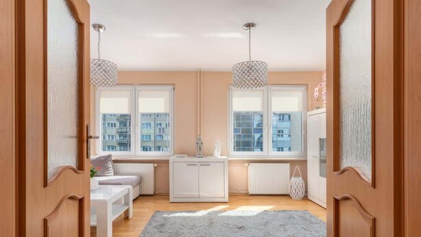 Un apartamento moderno con piso de madera, un sofá blanco, un tapete gris y un armario blanco.