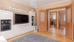 Una sala de estar moderna con televisor de pantalla plana, muebles blancos, alfombra gris y piso de madera.