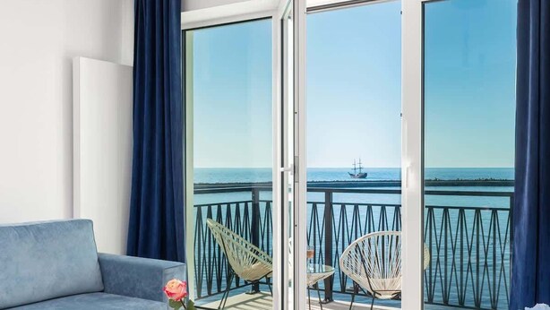 Ein modernes Wohnzimmer mit einer Couch, einem Glastisch und Meerblick durch große Fenster.
