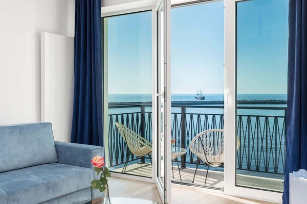 A bright living room with blue accents, featuring a cozy seating area and large windows overlooking the sea.