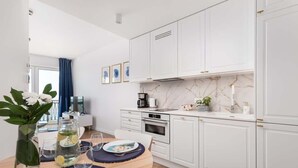 Eine moderne Küche mit weißen Schränken, einer Marmor-Spritzschutzleiste und einem Essbereich mit Holztisch und -stühlen.