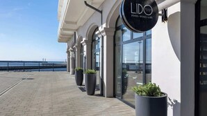 Ein Gebäude am Wasser mit einem Schild, auf dem 'LIDO BEACH CAFE FOOD WINE & LIRE' steht.