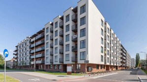 A modern multi-story apartment building with balconies, a bike lane, and a clear sky.