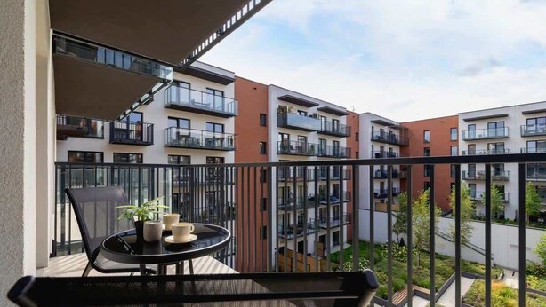 A balcony with a table and chairs, overlooking a residential area with multi-story buildings.