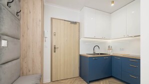 Een moderne keuken met witte en blauwe kastjes, een houten deur en een grijze bank.