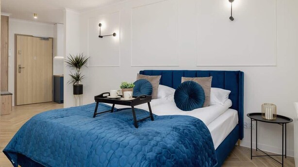 Een moderne slaapkamer met een groot bed, een nachtkastje, een wandlamp en een deur op de achtergrond.