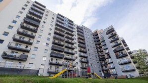 Een hoog appartementencomplex met meerdere balkons, een speelplaats en een gazon op de voorgrond.