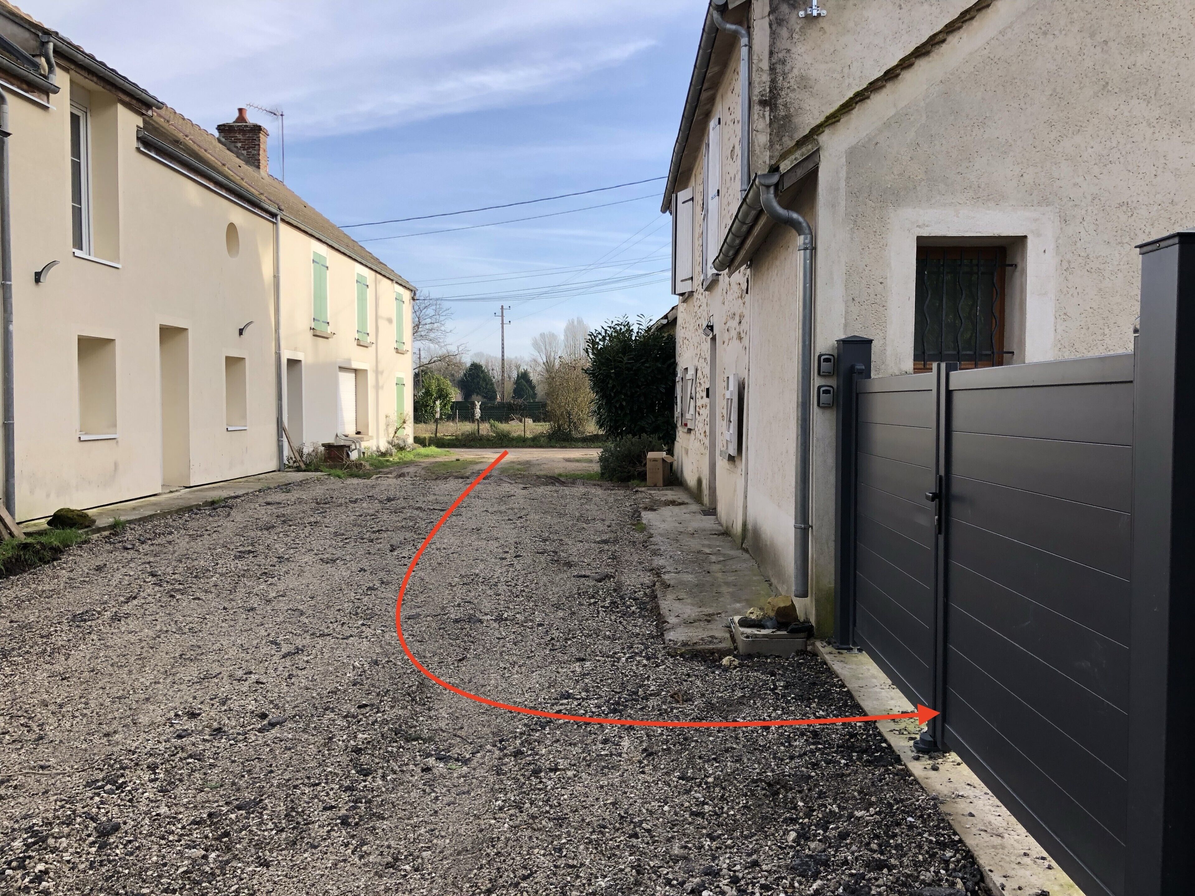 A narrow street with buildings on either side, a gravel path, and a closed gate.