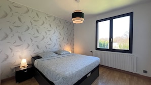 A modern bedroom with a bed, a nightstand, a wall-mounted lamp, a window with blinds, and a radiator. - La Graviere - Detached 28pers villa near Paris (Fontenay-Trésigny)