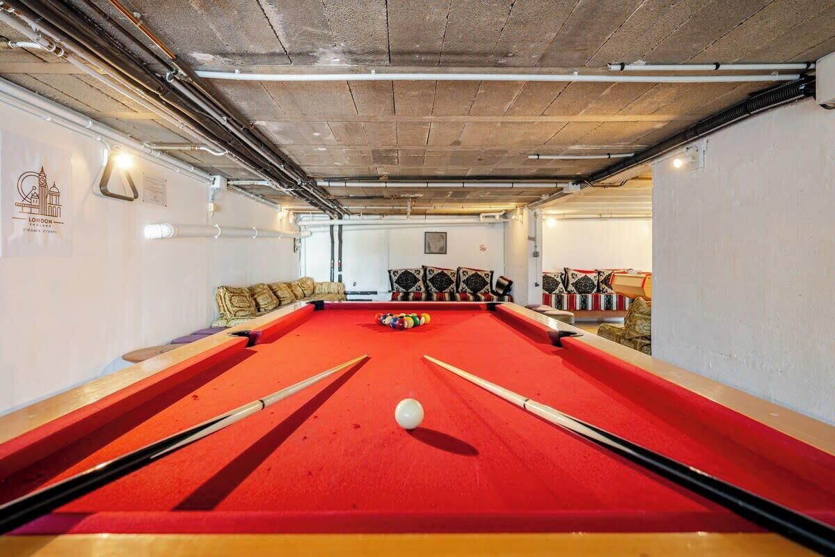 A pool table with a red felt surface, surrounded by cushions and pool cues.