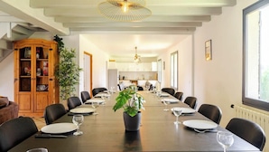 A dining area with a long table set for a meal, surrounded by chairs. There is a potted plant in the center of the table, and the room has a modern design with a ceiling light fixture above. - La Graviere - Detached 28pers villa near Paris (Fontenay-Trésigny)