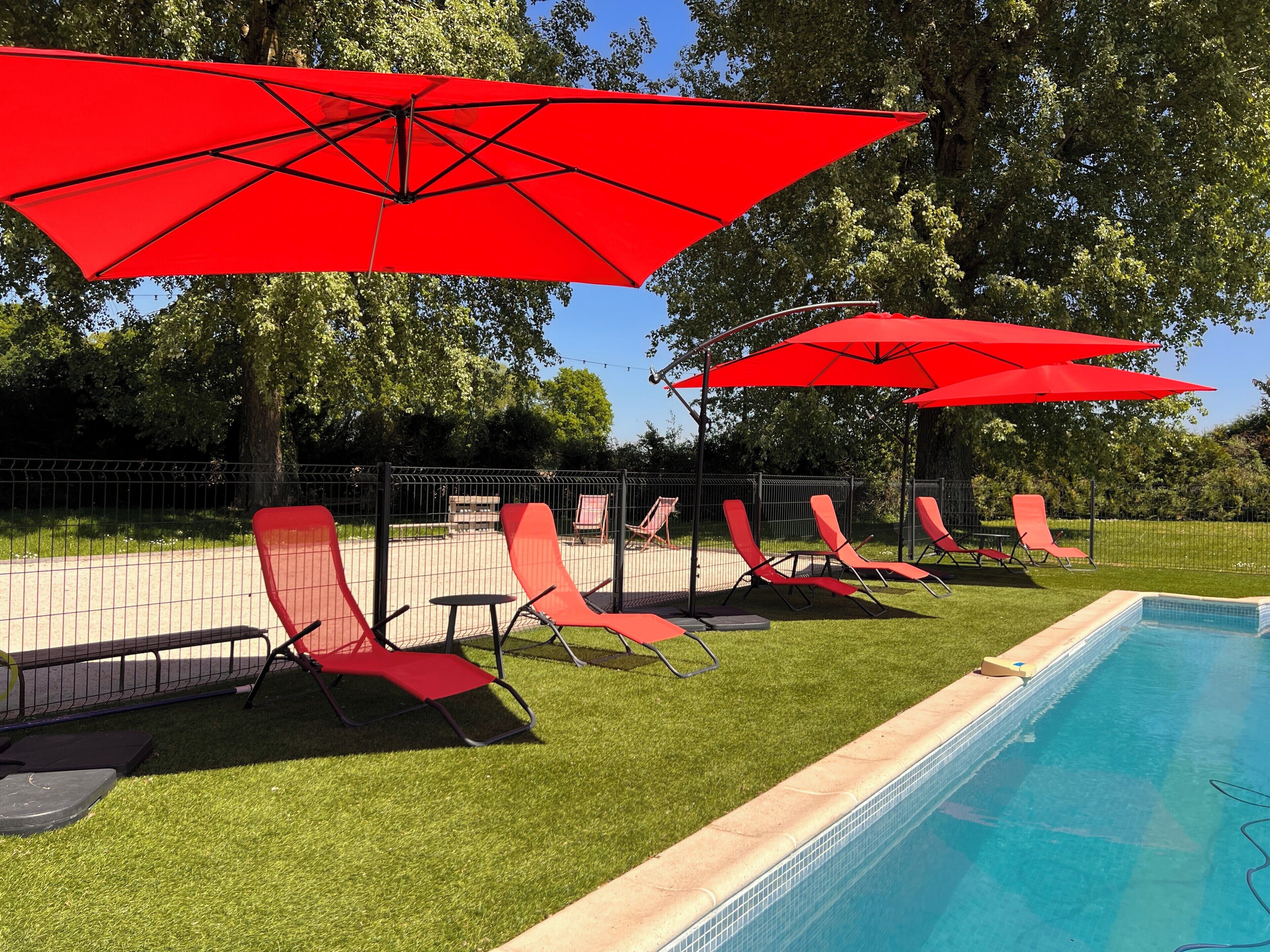 A poolside area with red umbrellas, lounge chairs, and a clear blue pool.