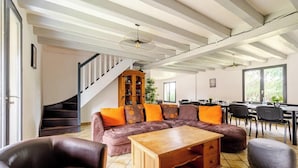 A spacious living room with a large sectional sofa, a wooden coffee table, and a staircase leading to an upper floor. - La Graviere - Detached 28pers villa near Paris (Fontenay-Trésigny)