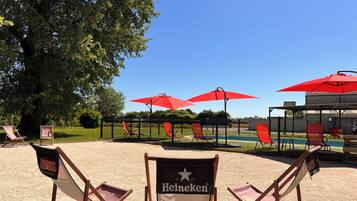 Un espace aménagé avec des chaises à l’effigie de la marque Heineken, des parasols rouges et une piscine en arrière-plan.