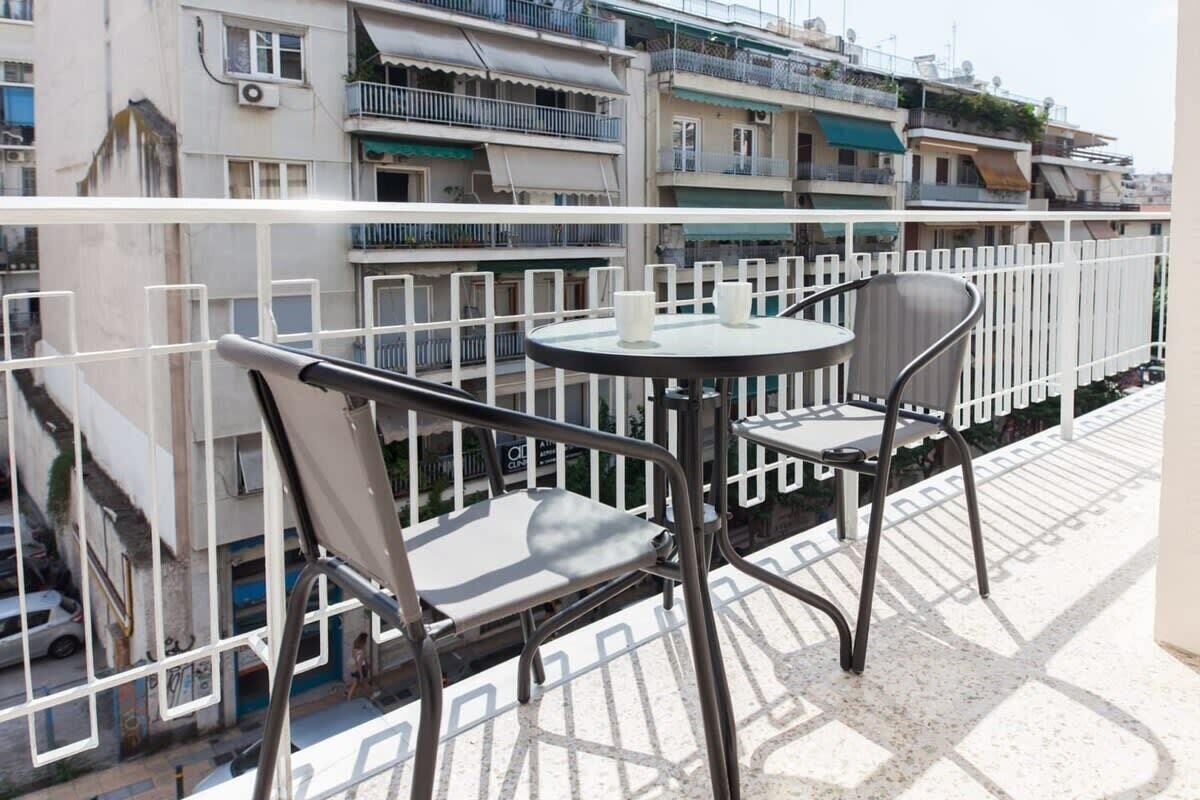 A balcony with a round table and two chairs, overlooking a residential area with multi-story buildings.
