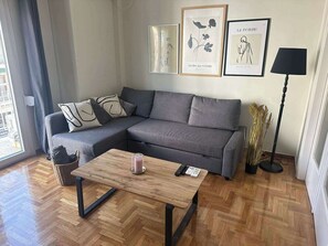 Uma sala de estar moderna com um sofá seccional cinza, uma mesa de centro de madeira e um abajur. Há quadros na parede e uma janela com cortinas.