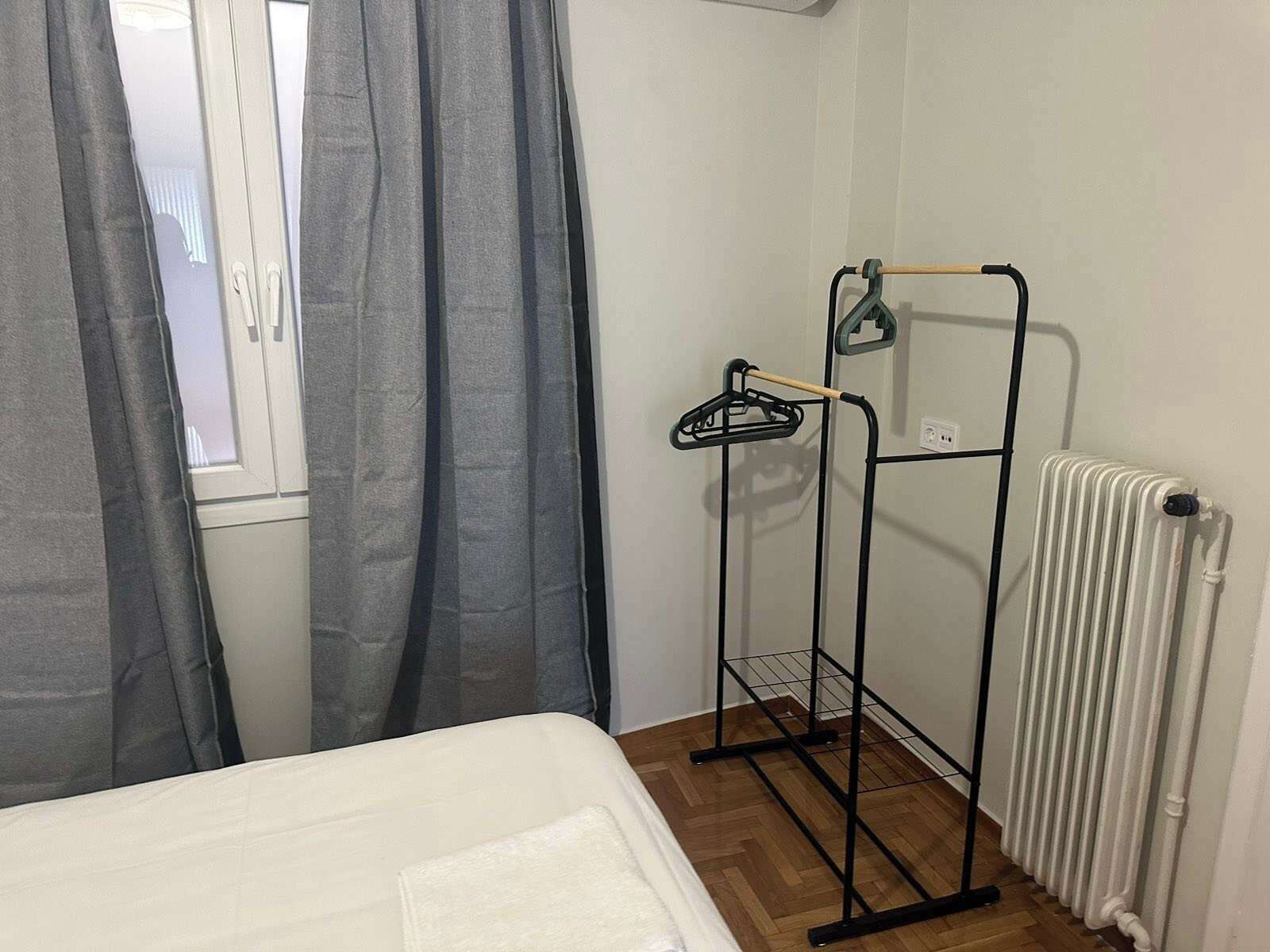 Quarto com cama, radiador e cabideiro.