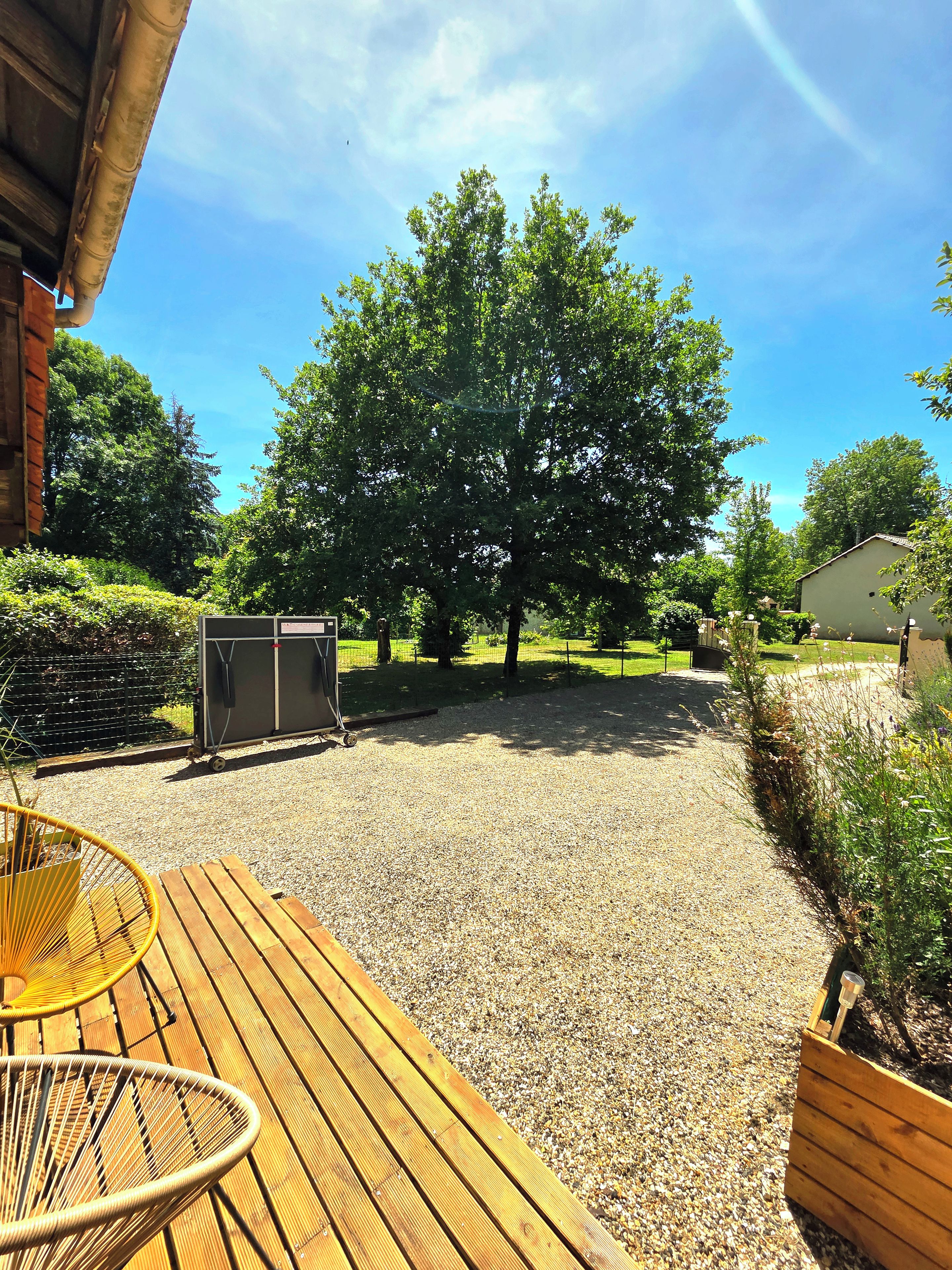A wooden deck with a chair, a gravel area, and a large tree in the background.