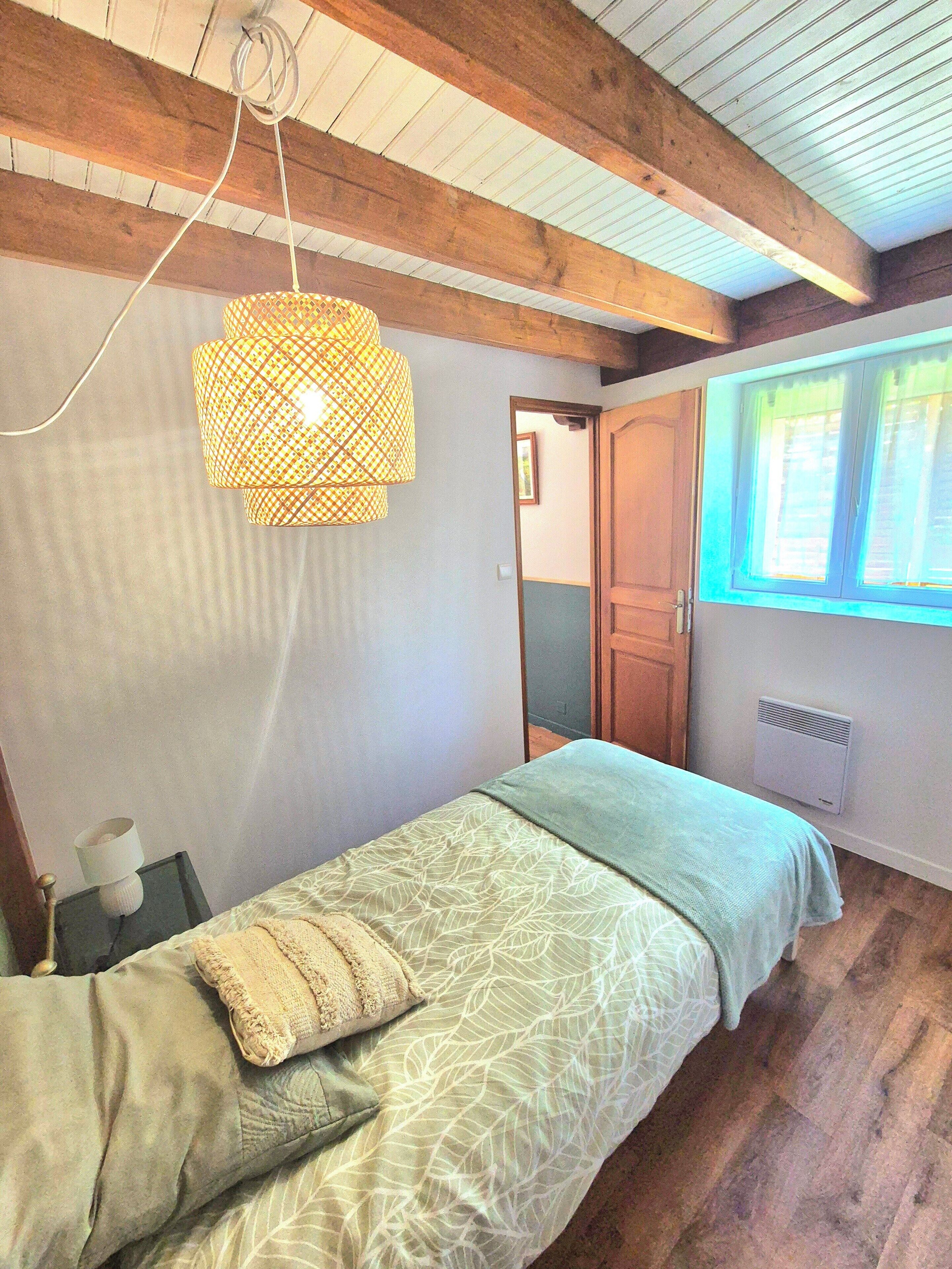 A bedroom with a bed, a hanging light fixture, a radiator, and a window with curtains.