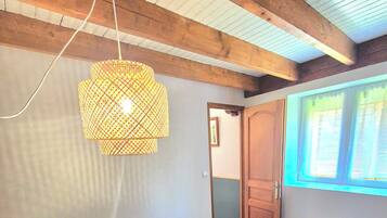 A bedroom with a bed, a hanging light fixture, a radiator, and a window with curtains.