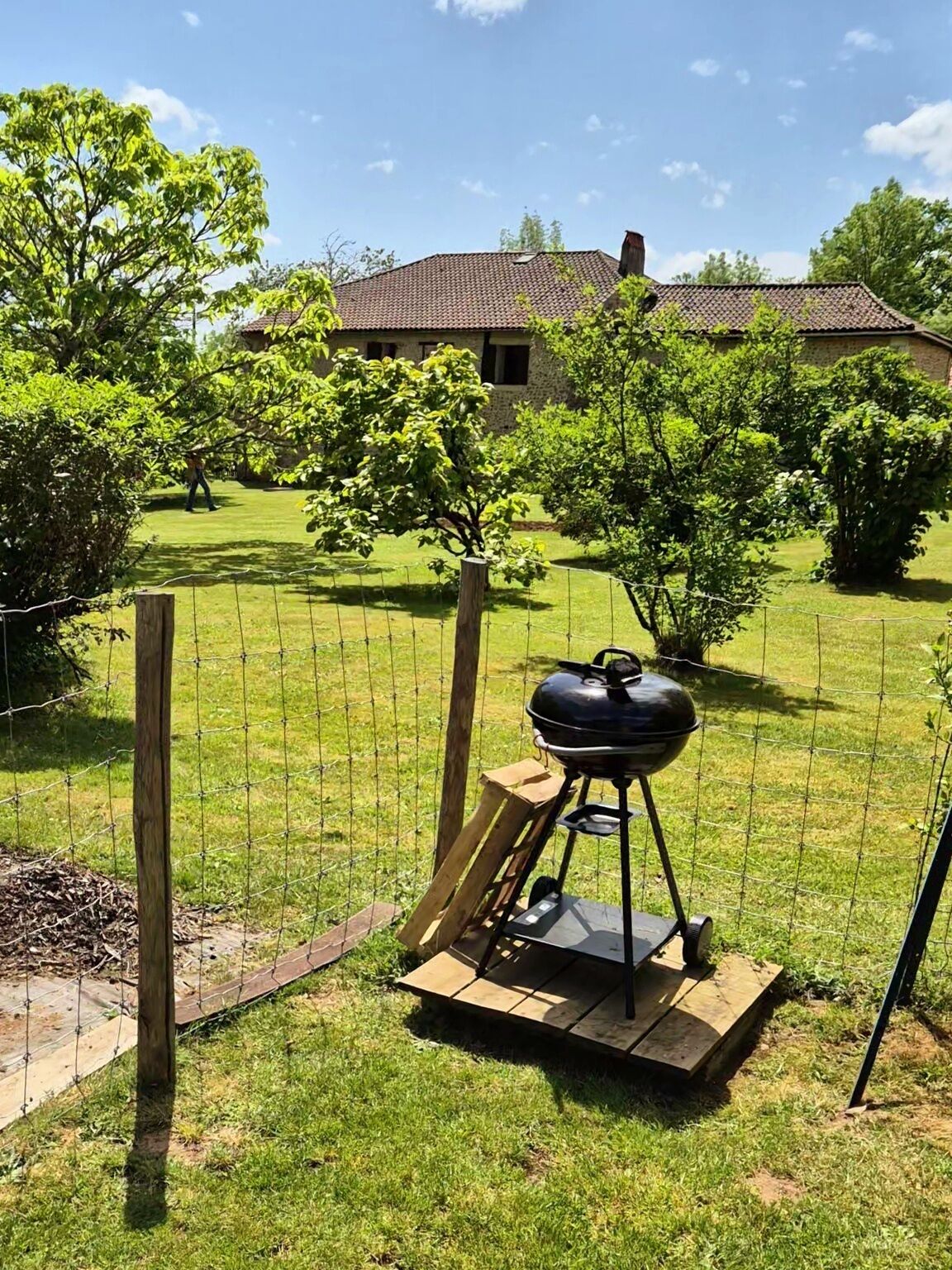 Een achtertuin met een barbecue, houten omheining en een huis op de achtergrond.
