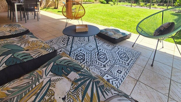 Une terrasse extérieure dotée d’un plafond en bois, d’une table à manger avec des chaises, et d’un espace gazonné agrémenté d’arbres.