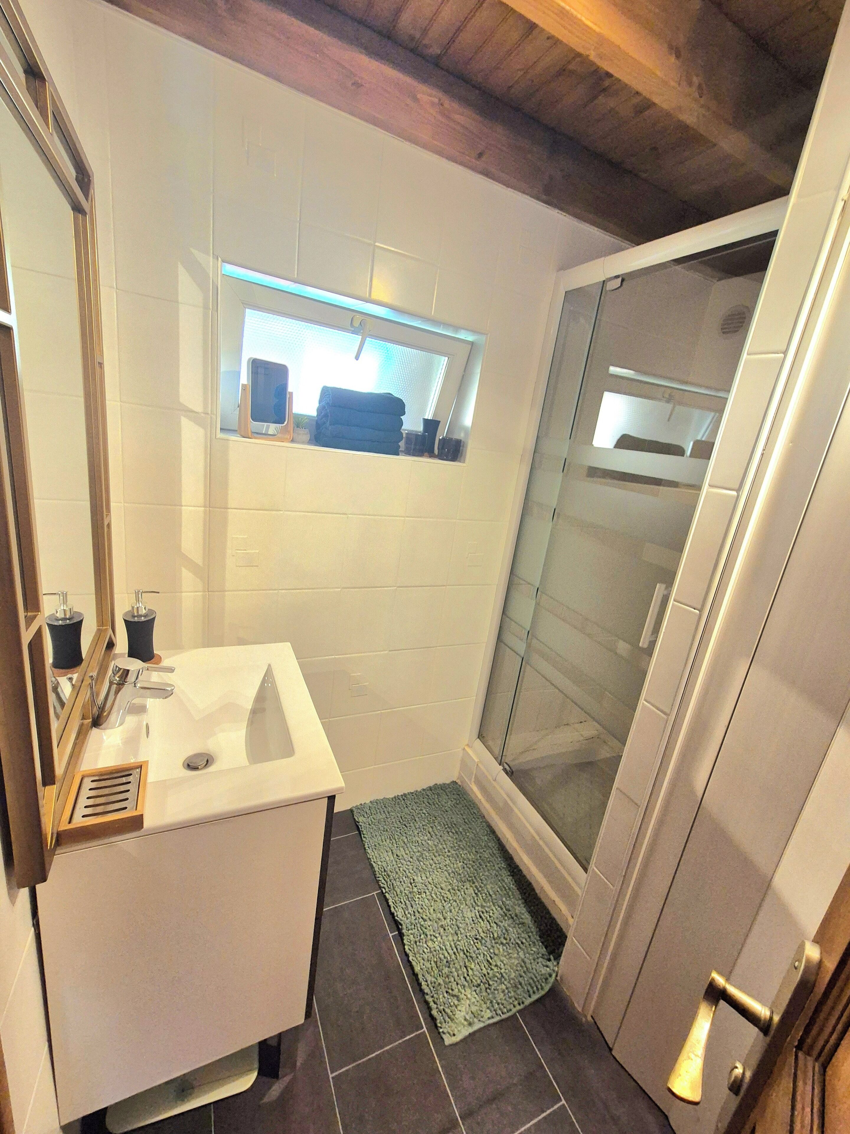 A bathroom with a white sink, a mirror, a window, and a shower area.