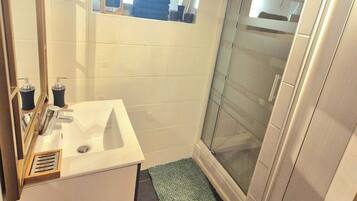 A bathroom with a white sink, a mirror, a window, and a shower area.