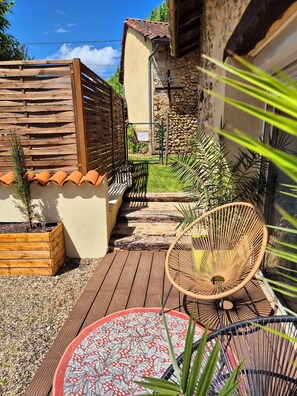 Una terraza de madera con una silla tejida, una mesa estampada y un muro de piedra.