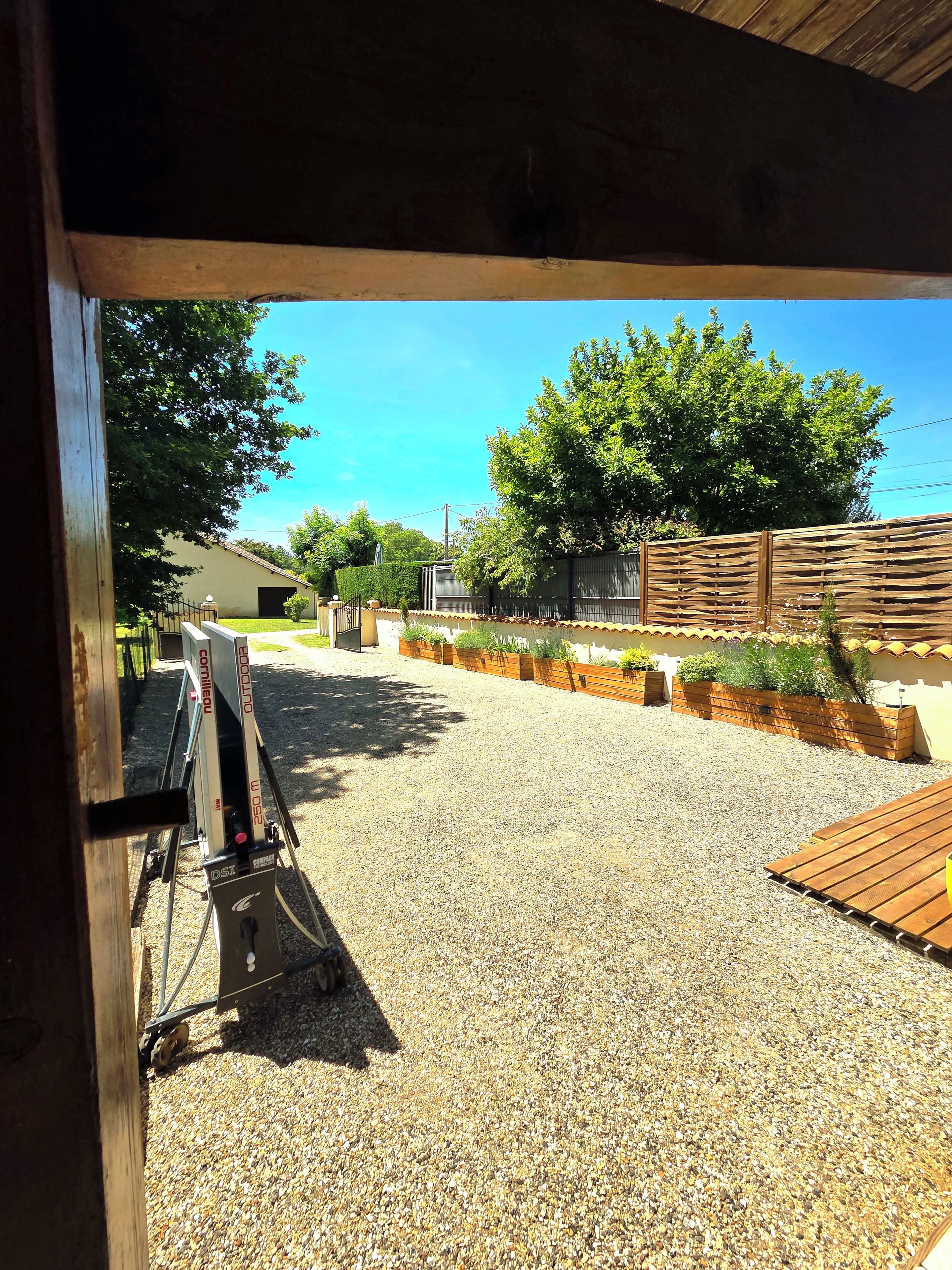 An outdoor area with a gravel surface, wooden deck, and a fenced garden area.