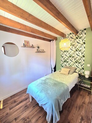 Une chambre à coucher avec un lit, un luminaire suspendu, un miroir et un mur orné d’un motif de feuilles.