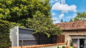 Un jardin clos, avec un chemin de gravier, des jardinières en bois et un bâtiment doté d’un toit en tuiles.