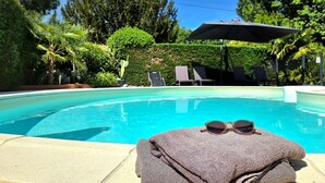 Une piscine dotée de chaises longues et d’un espace abrité, le tout entouré de verdure.