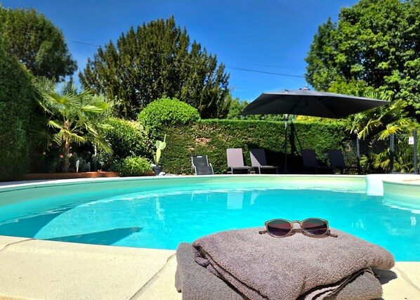 Une piscine dotée de chaises longues et d’un espace abrité, le tout entouré de verdure.