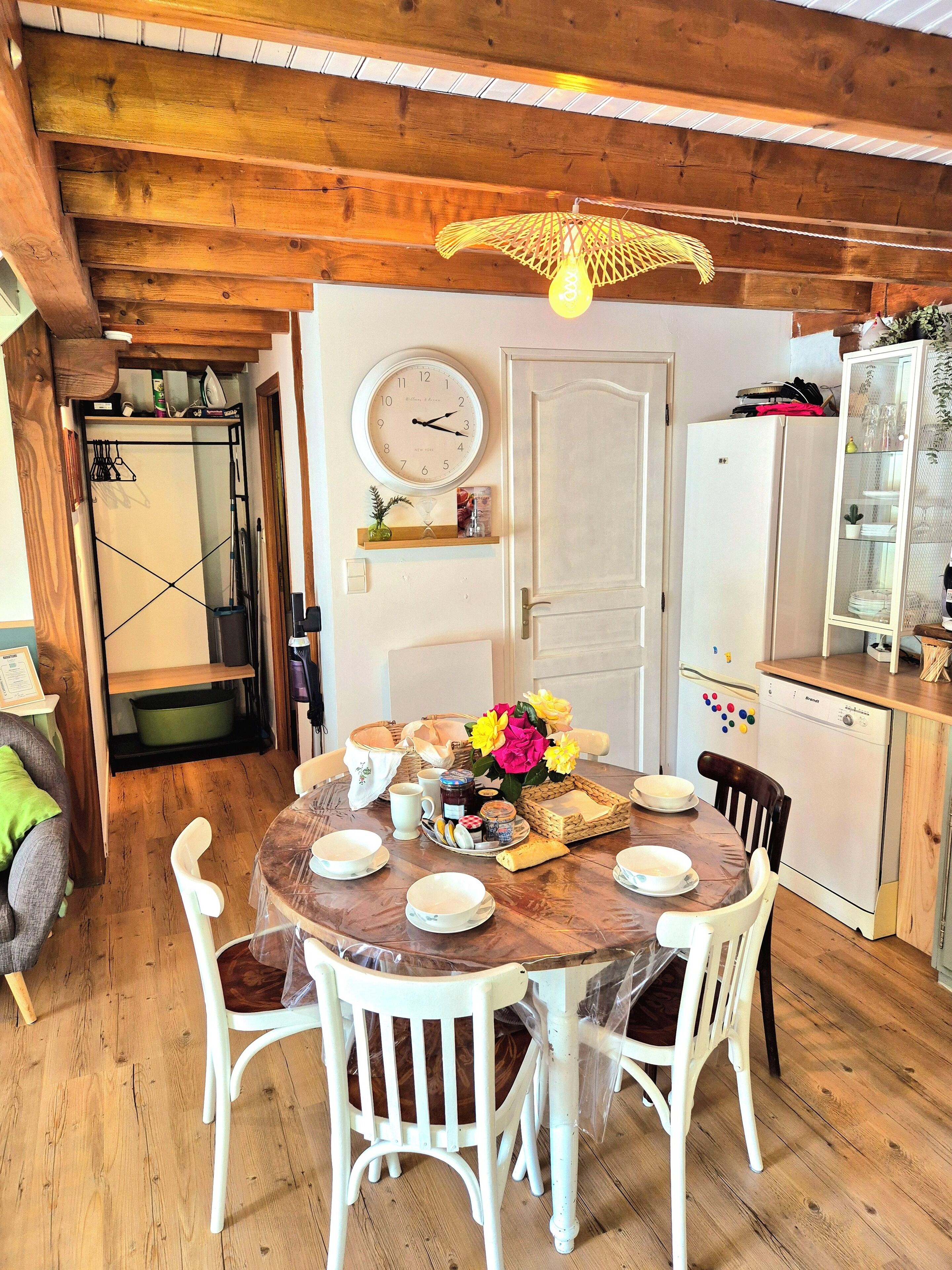 A wooden dining table with chairs, a clock, and a refrigerator in a kitchen area.