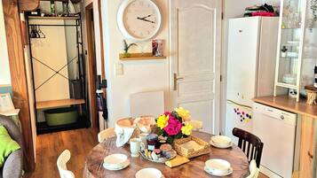 A wooden dining table with chairs, a clock, and a refrigerator in a kitchen area.