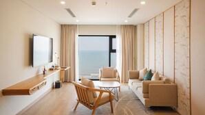 A modern living room with a flat-screen TV, wooden furniture, a sofa, and a view of the sea. - Seabird Hotel Thien Cam (Thiên Cầm)