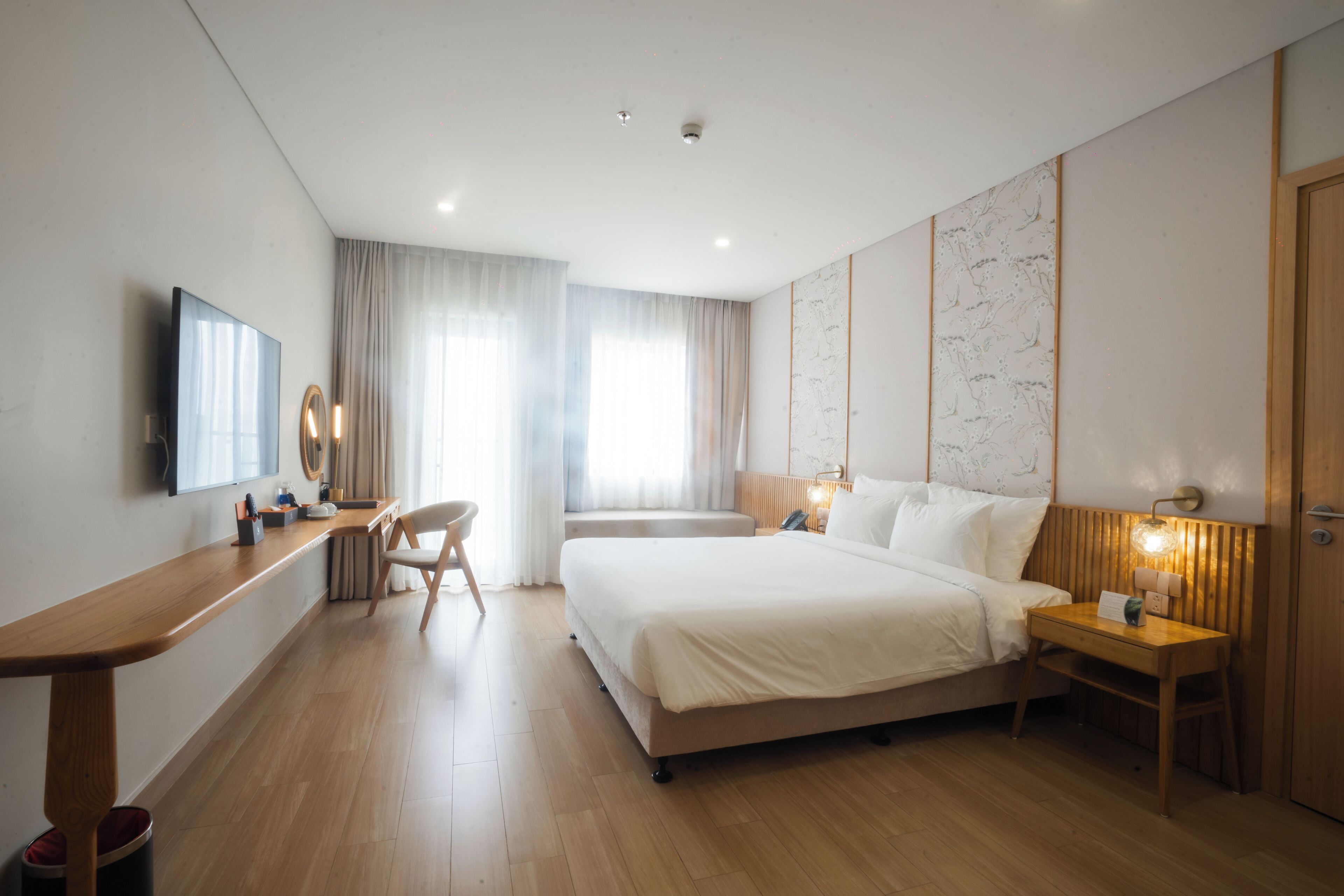 Ein modernes Hotelzimmer mit Schreibtisch aus Holz, einem Bett, einem Nachttisch und einem Fernseher.