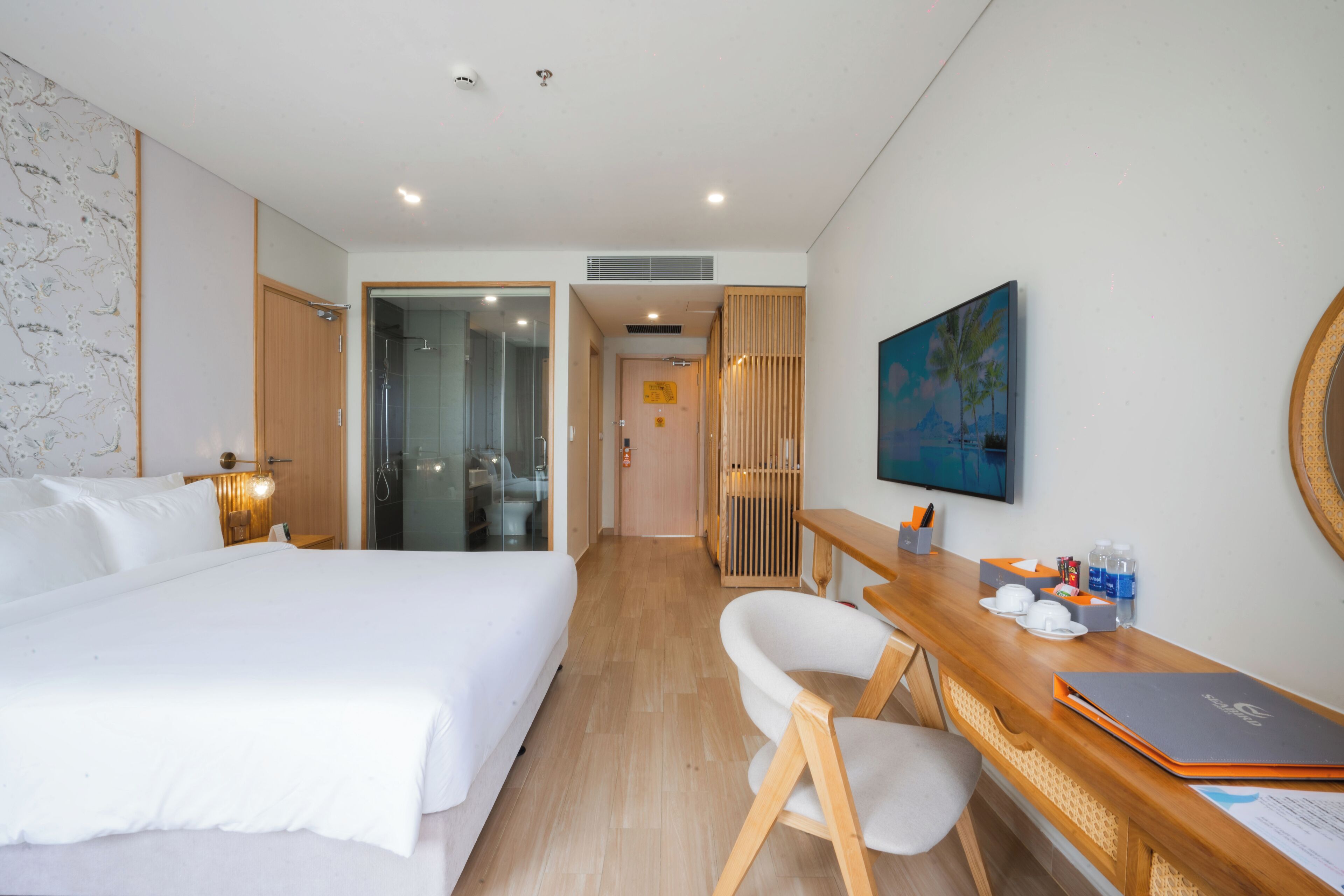 Habitación de hotel con cama, escritorio con silla, un cuadro en la pared y una puerta de madera que da a otra habitación.