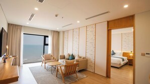 A modern hotel room with a large window, a sofa, a wooden chair, a small table, and a bed. - Seabird Hotel Thien Cam (Thiên Cầm)