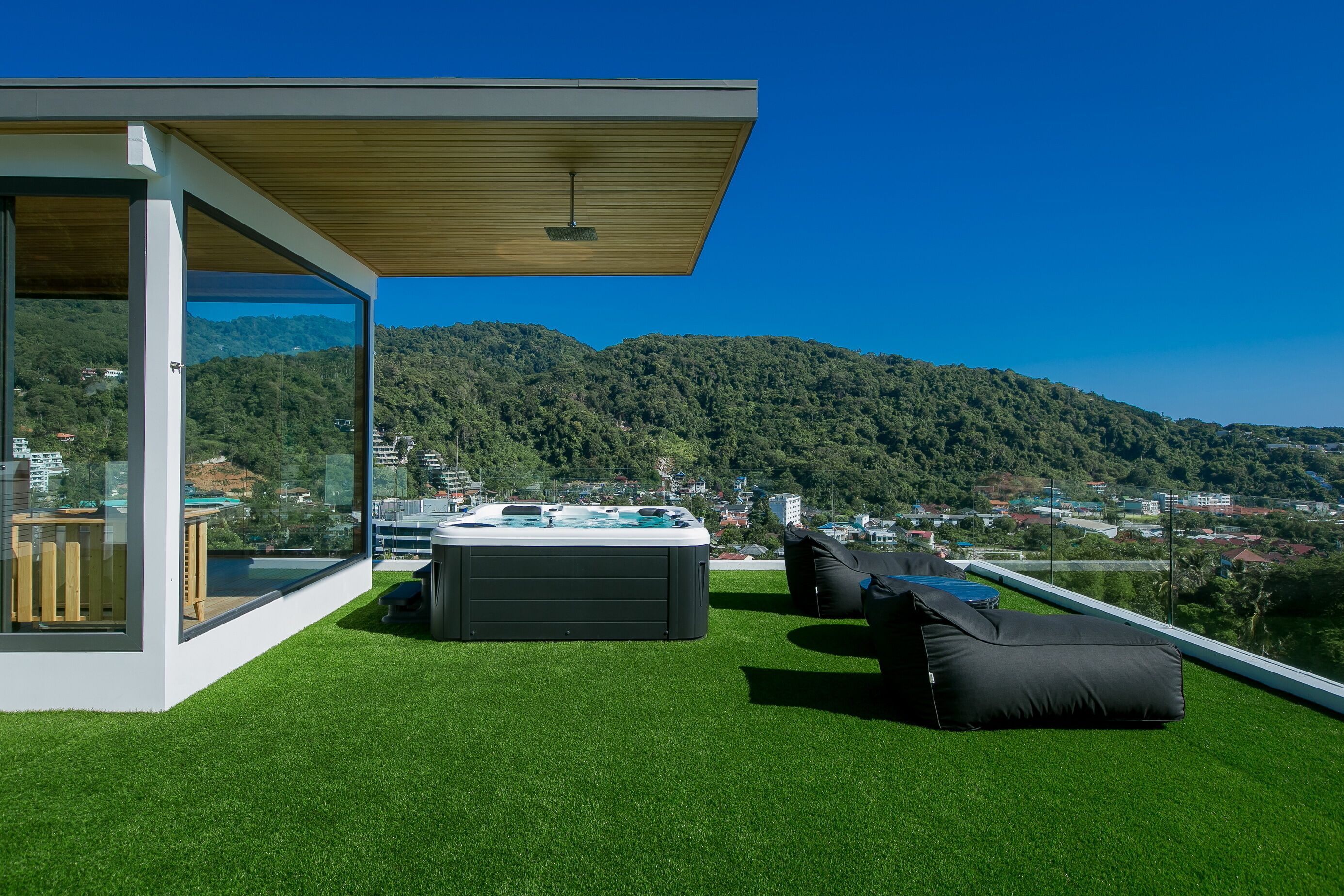 A modern outdoor space with a hot tub, seating, and a glass door leading to a deck.