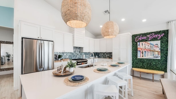 A modern kitchen with white cabinets, a stainless steel refrigerator, and a central island with bar stools.