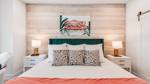A bedroom with a wooden headboard, a bed with a white and pink bedspread, leopard print pillows, and two bedside tables with lamps.